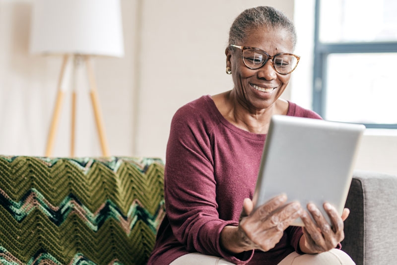 An elderly woman sits on a couch looking at a tablet