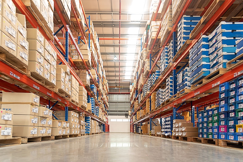 An aisle in a large warehouse showing shelves fully stocked with items