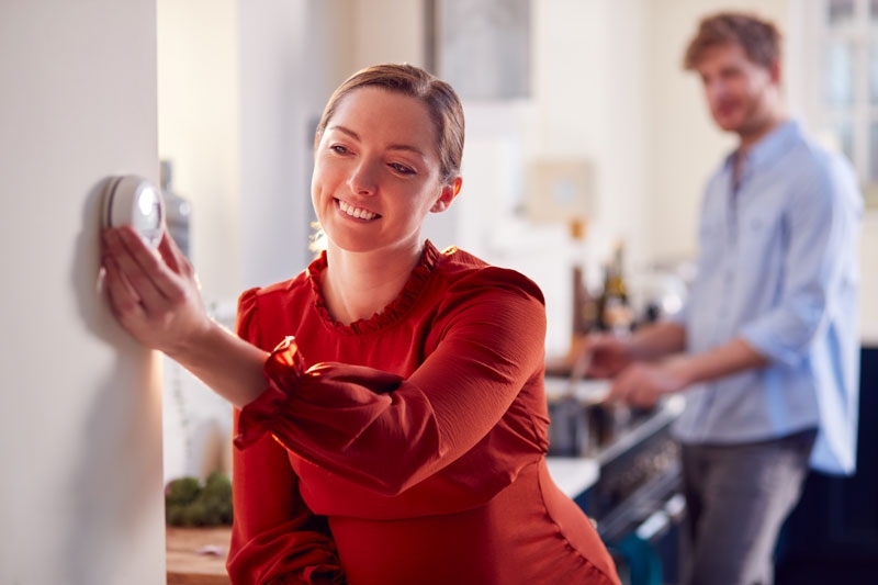 a woman in her home adjusts a smart thermostat on the wall
